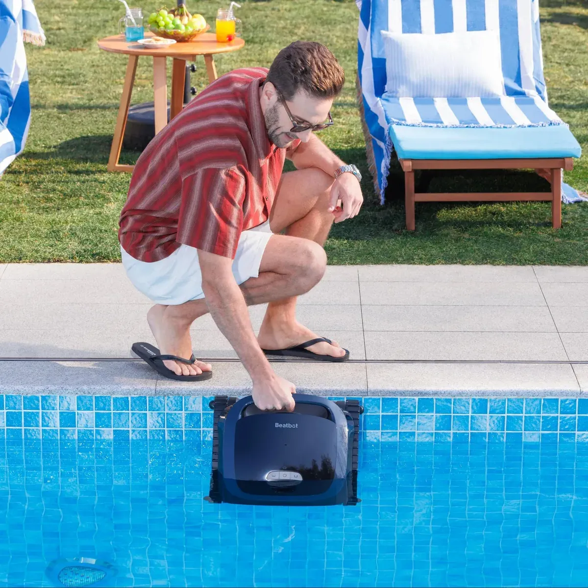 A person crouching at the pool edge lowers a Beatbot AquaSense 2 into the water