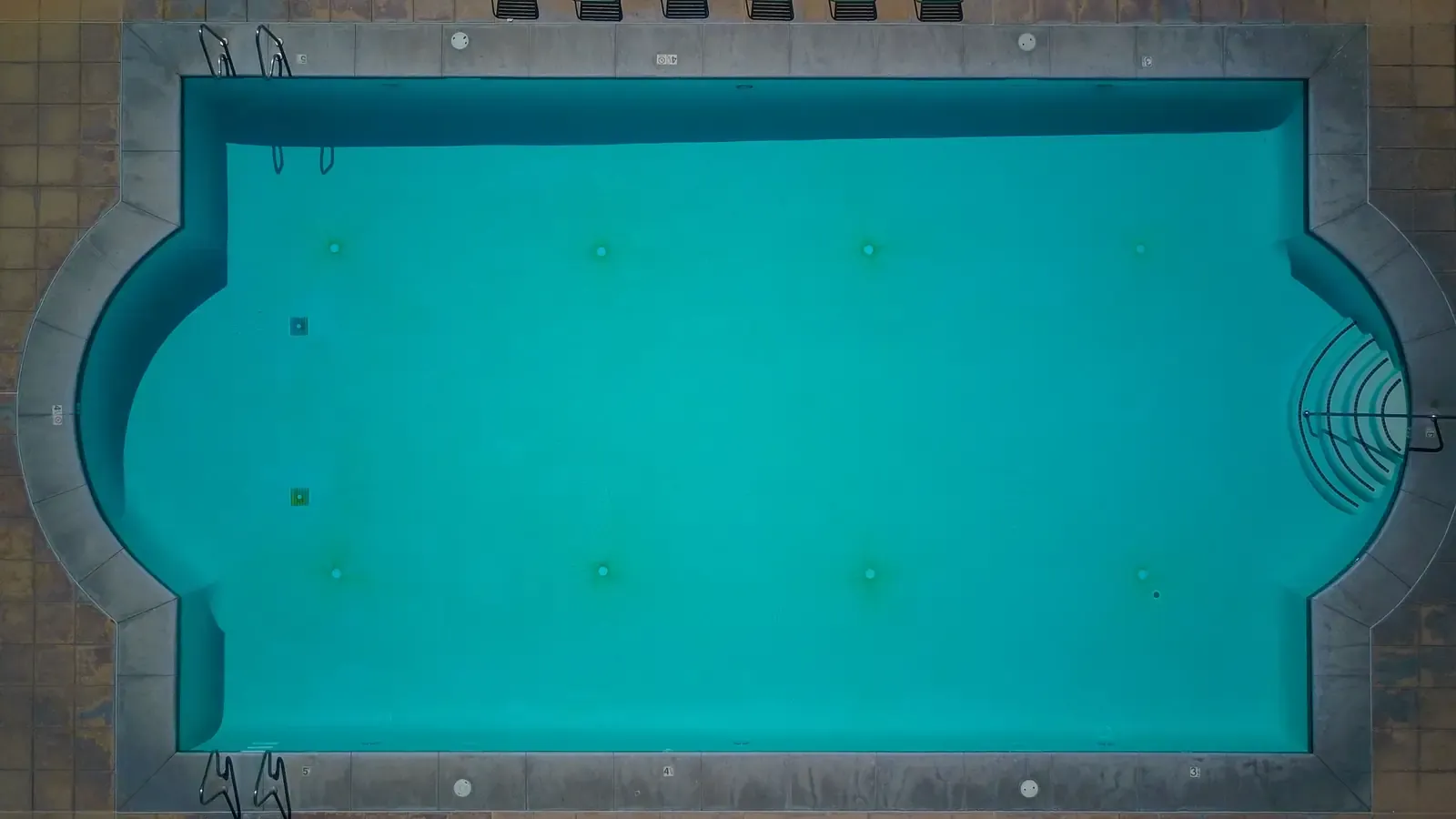 Top-down view of a rectangular in-ground pool with rounded ends, clear turquoise water and steps at one end